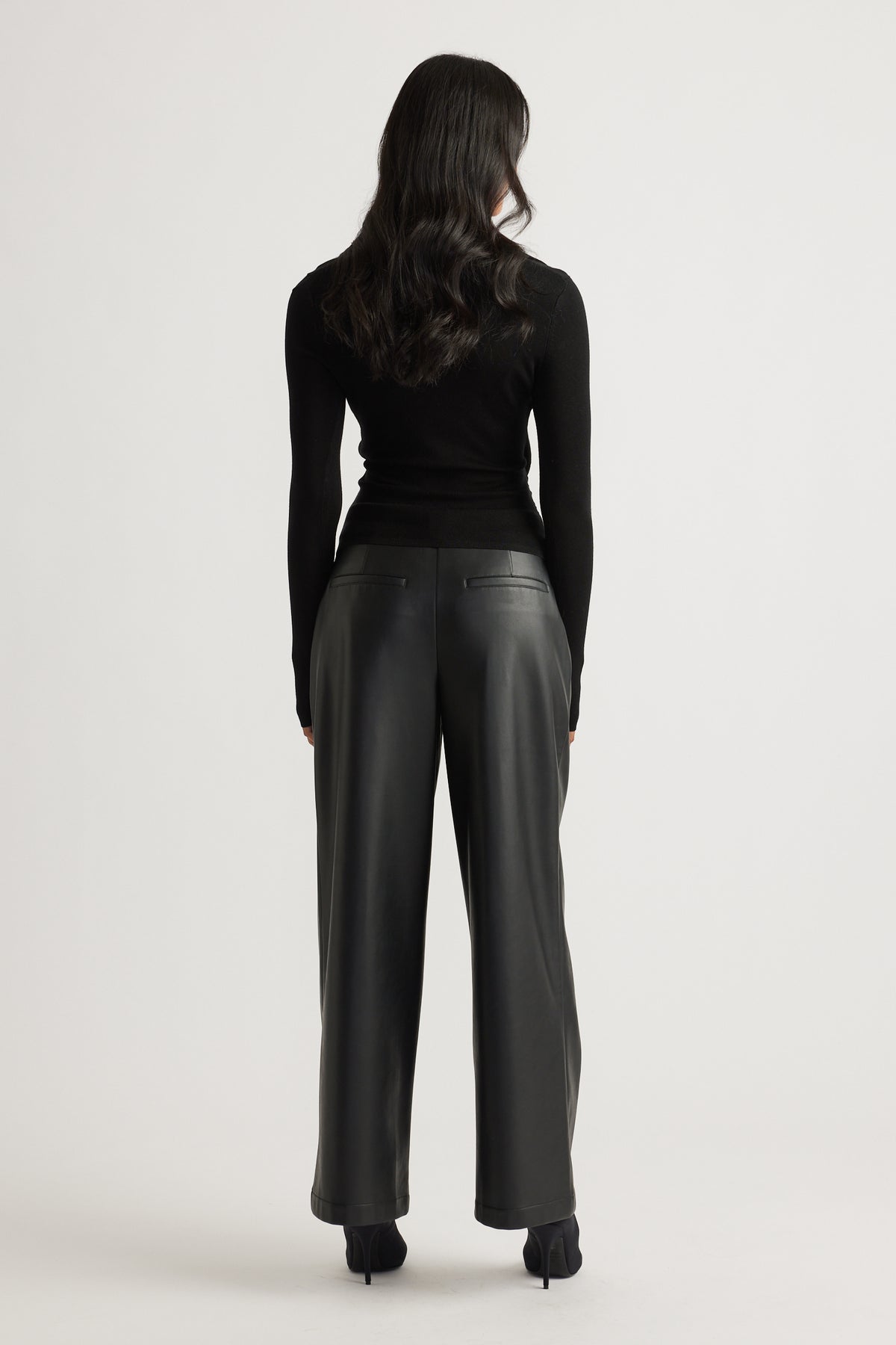 Woman wearing a fitted black knit top with long sleeves paired with high-waisted wide-leg black leather pants