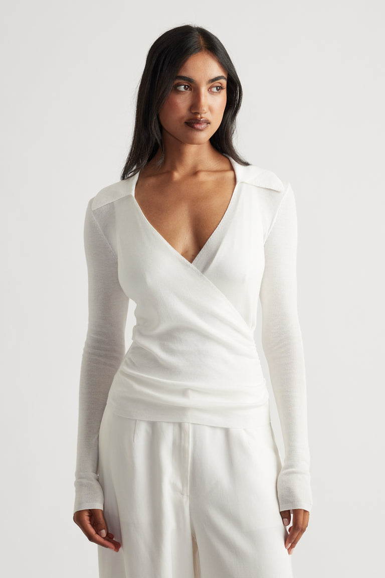 Woman wearing an elegant white crossover fine knit top with long sleeves and relaxed white pants for a polished look