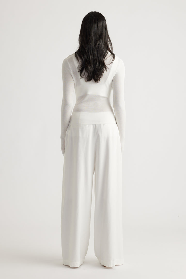 Woman wearing a soft white fine knit top with a crossover detail paired with loose wide-leg trousers for a relaxed look