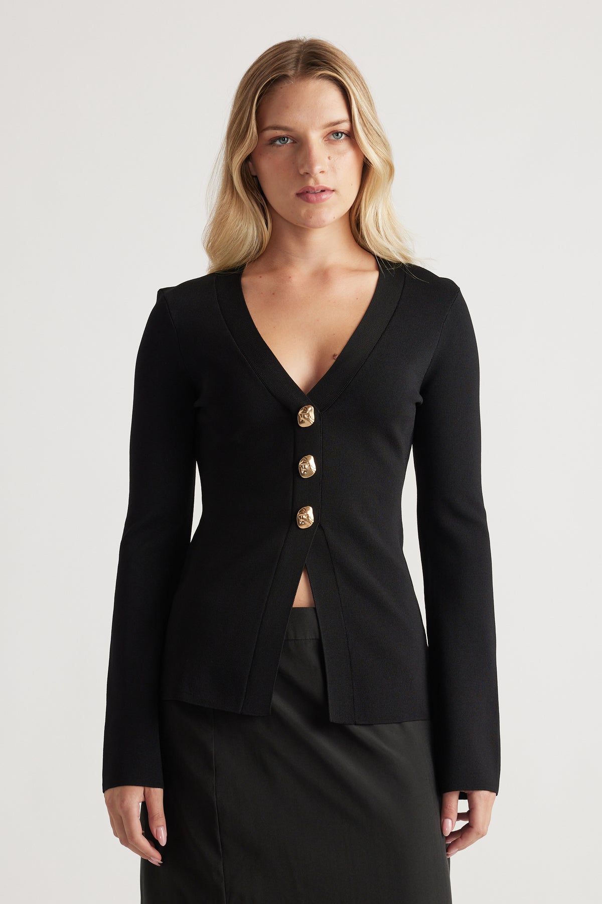 Woman wearing a fitted black longline cardigan with gold buttons, featuring a deep V-neck and long sleeves