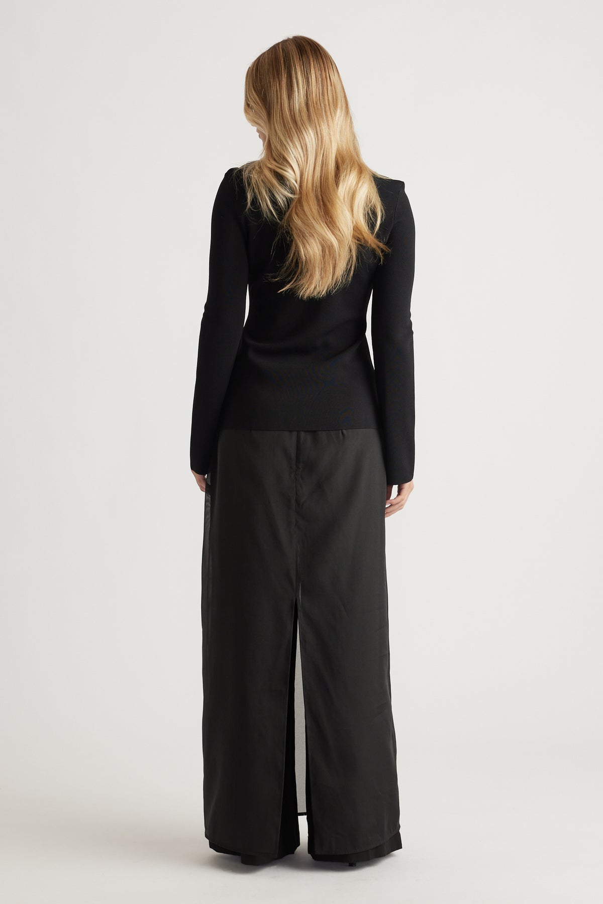 Woman wearing a fitted black long-sleeve top paired with a high-waisted, back-slit maxi skirt in black