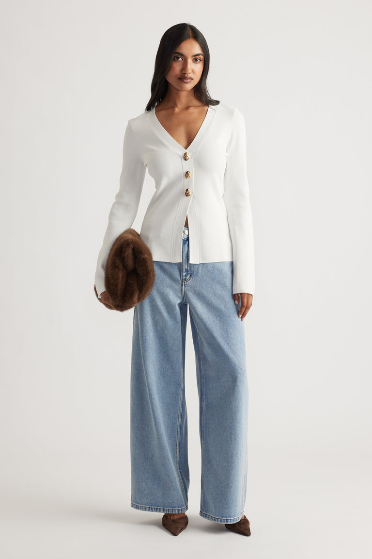 Woman wearing a fitted ivory knit cardigan with tortoiseshell buttons paired with wide-leg light blue denim jeans