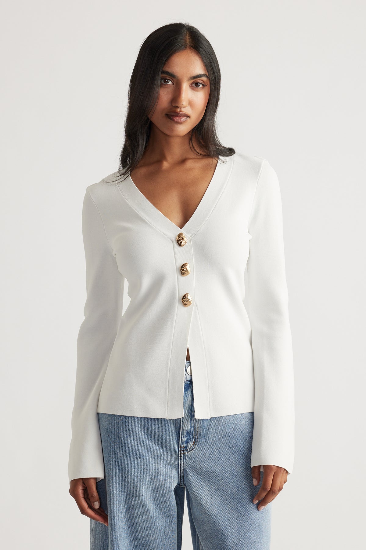 Woman wearing an ivory longline knit cardigan with gold buttons, styled with relaxed light blue denim jeans