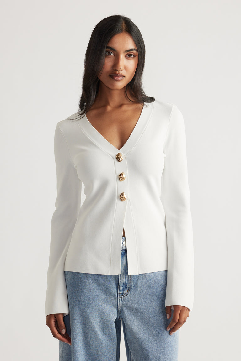 Woman wearing an ivory longline knit cardigan with gold buttons, styled with relaxed light blue denim jeans