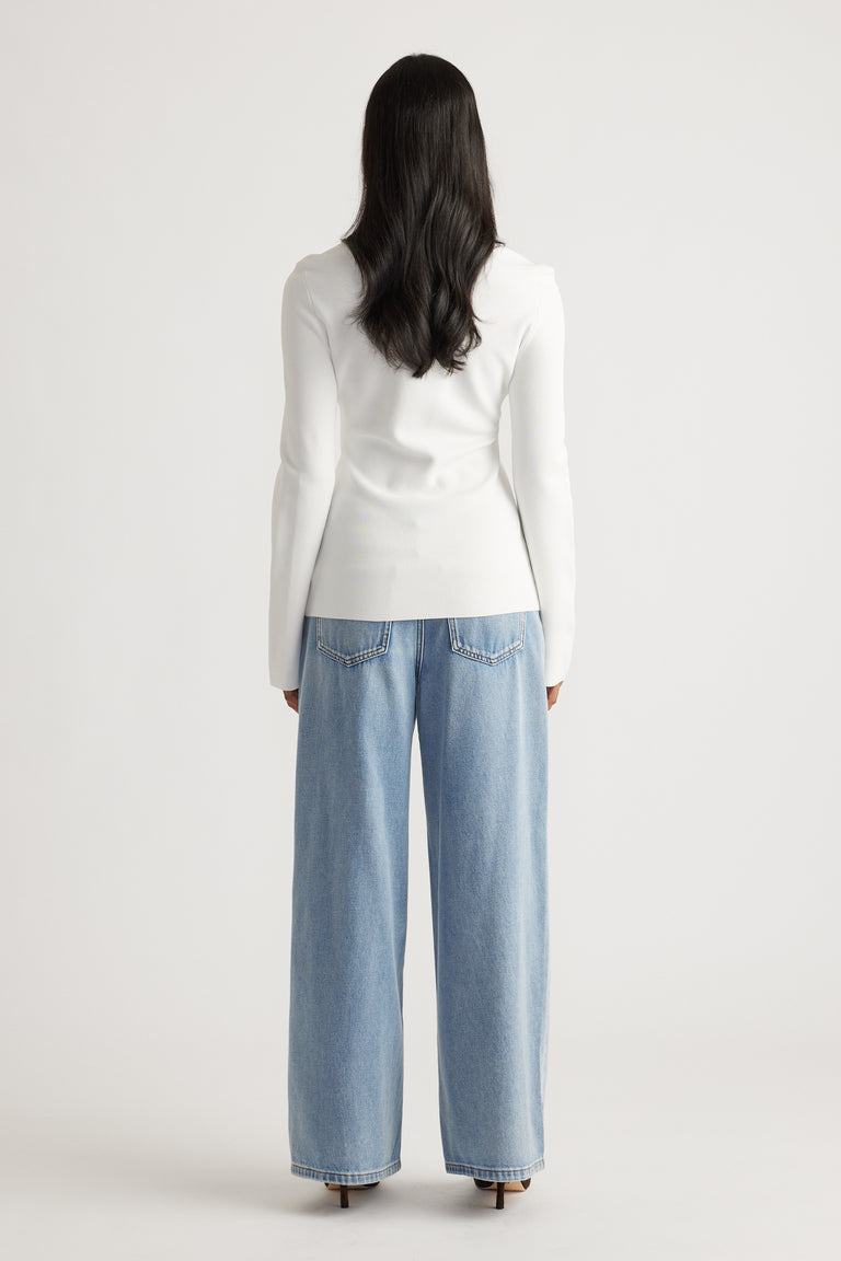 Woman wearing a fitted white long-sleeve top paired with loose wide-leg light blue denim jeans from behind viewpoint