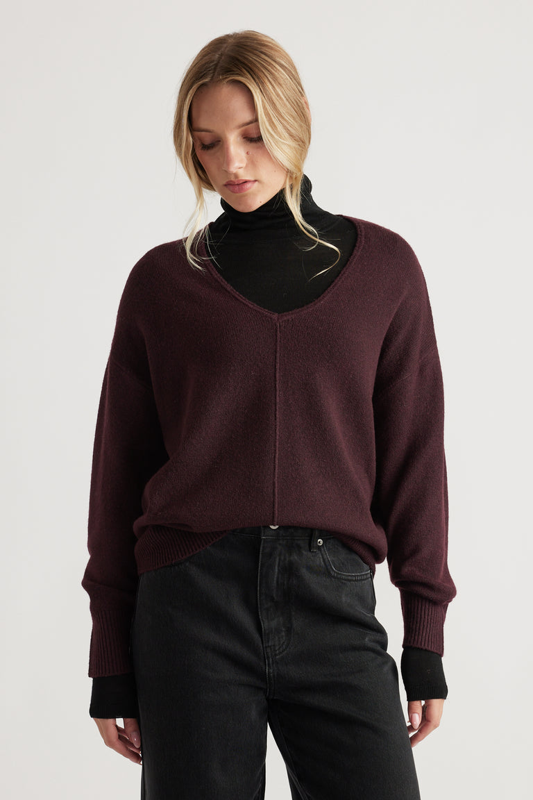 Woman wearing a deep burgundy knit jumper with seam detail over a black turtleneck and high-waisted black jeans