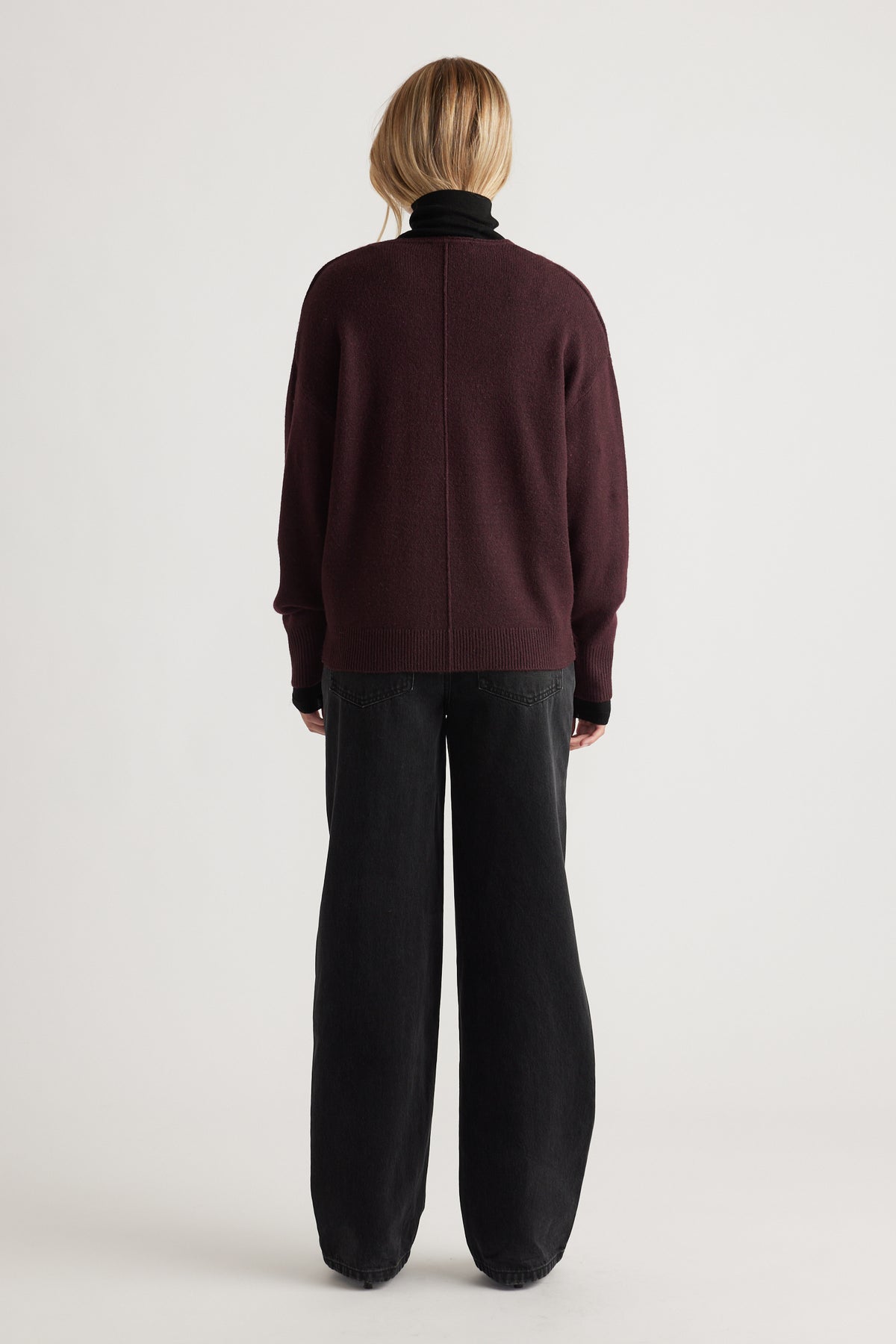 Back view of a deep burgundy knit sweater with subtle seam detail paired with loose-fitting black pants