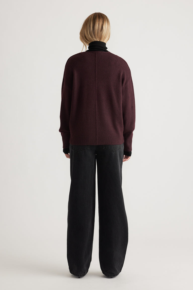 Back view of a deep burgundy knit sweater with subtle seam detail paired with loose-fitting black pants