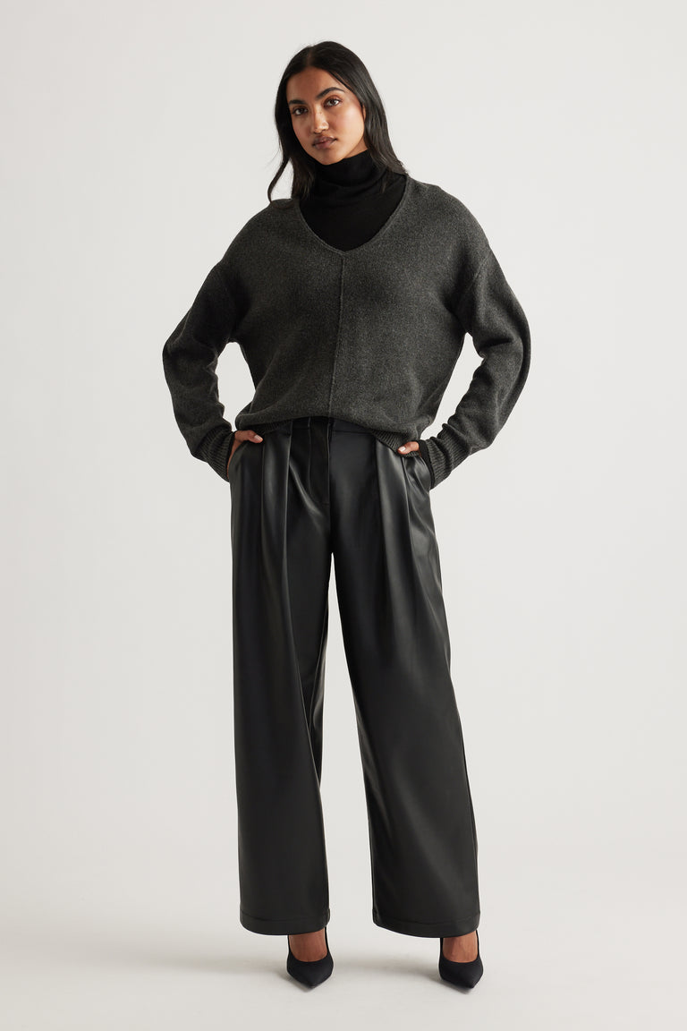 Woman wearing a charcoal knit jumper with a deep V-neck and seam detail, paired with black wide-leg trousers and heels