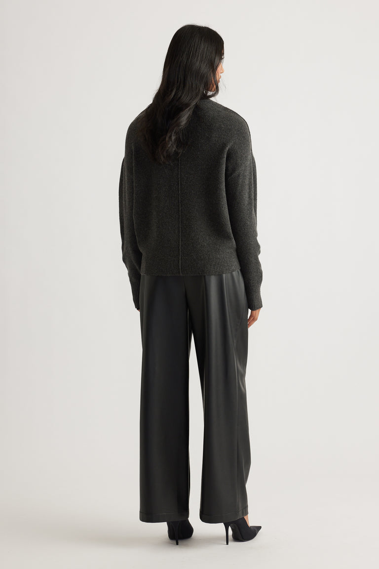 Woman wearing a charcoal knit jumper with subtle seam detail, paired with black wide-leg leather-look pants and heels