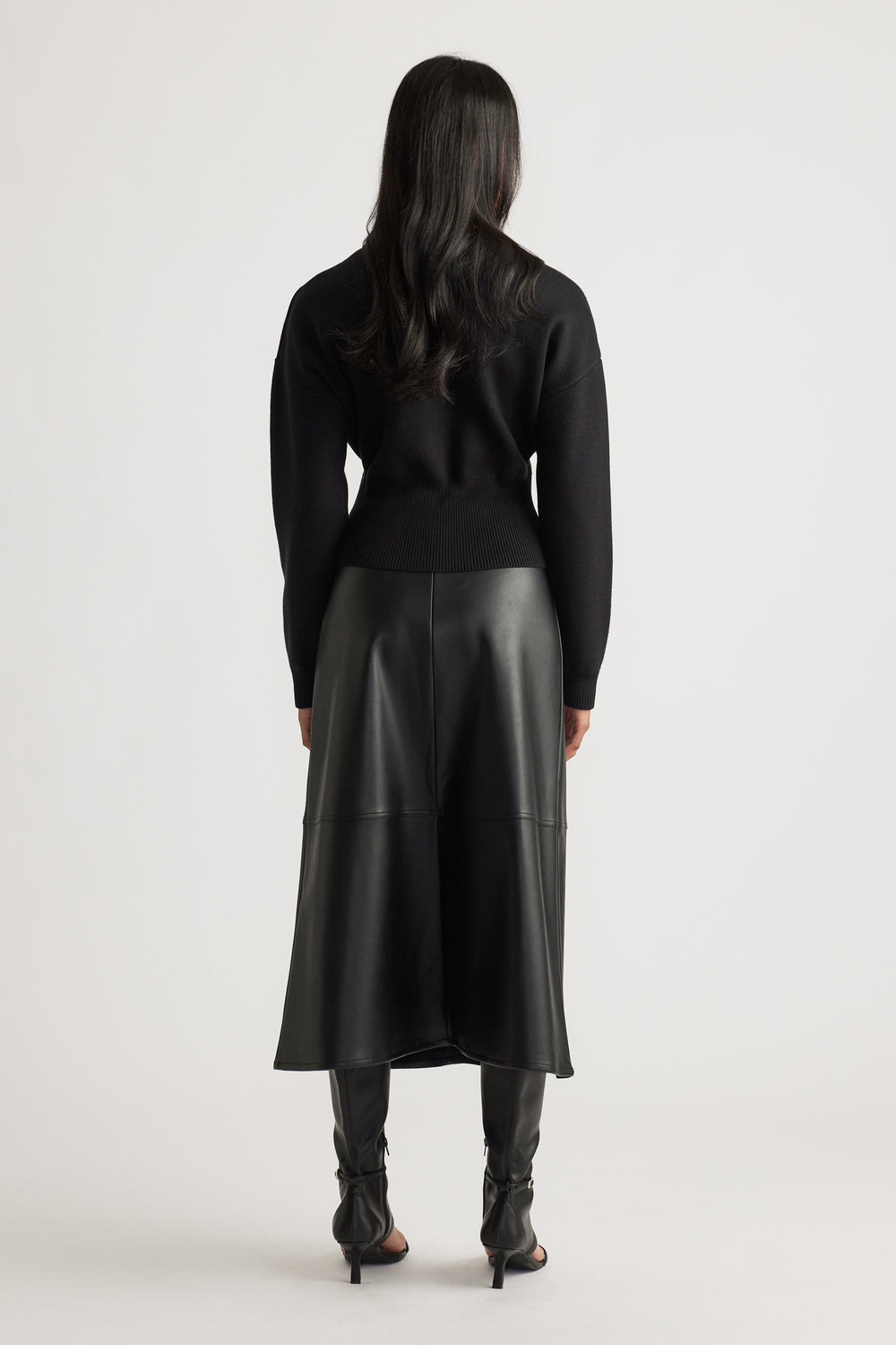 Woman wearing a fitted black knit bomber with ribbed hem, paired with a black faux leather midi skirt and heeled boots