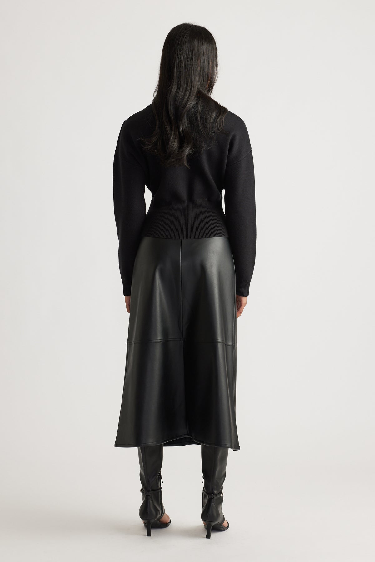 Woman wearing a fitted black knit bomber with ribbed hem, paired with a black faux leather midi skirt and heeled boots