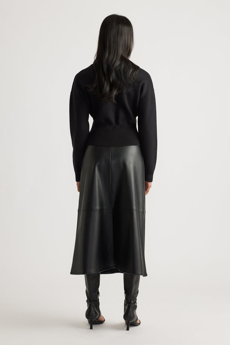 Woman wearing a fitted black knit bomber with ribbed hem, paired with a black faux leather midi skirt and heeled boots