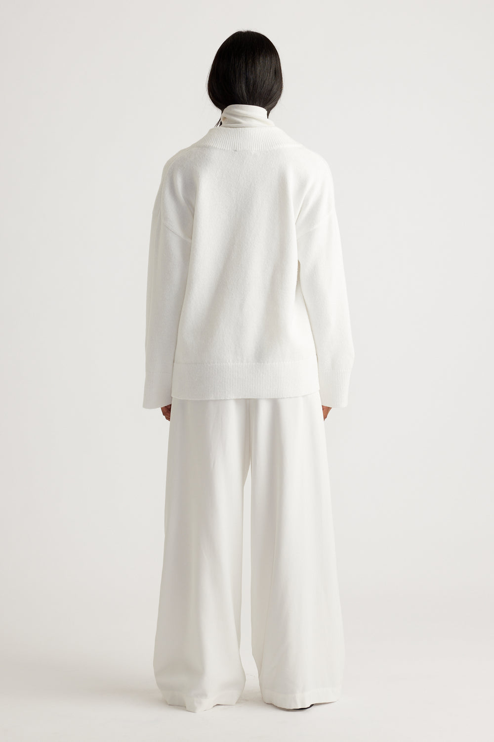 Woman wearing an oversized white knit sweater paired with wide-leg trousers for a relaxed, minimalist look