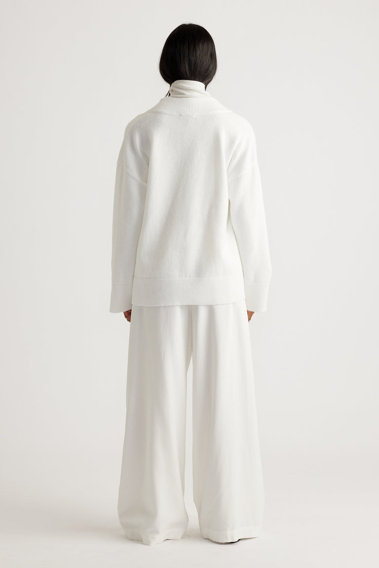 Woman wearing an oversized white knit sweater paired with wide-leg trousers for a relaxed, minimalist look