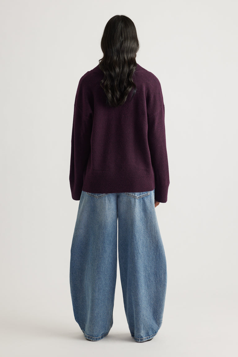 Woman seen from behind wearing a deep burgundy v-neck knit jumper paired with loose wide-leg denim jeans