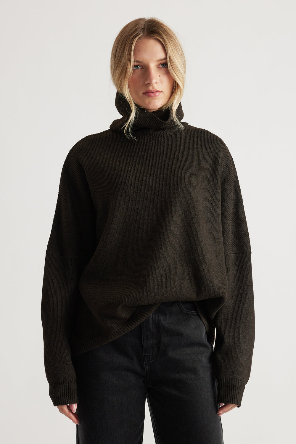 Woman wearing a dark brown roll neck jumper with a relaxed fit paired with high-waisted black jeans for a minimalist look