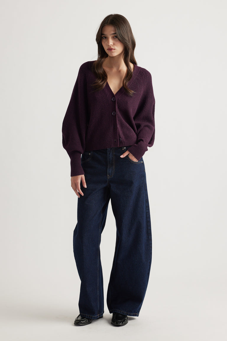 Woman wearing a deep burgundy knit cardigan with balloon sleeves paired with wide-leg dark denim jeans and black shoes