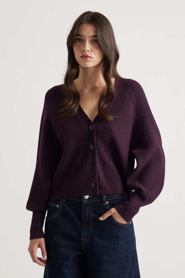 Woman wearing a deep plum knit cardigan with balloon sleeves paired with dark blue wide-leg denim jeans