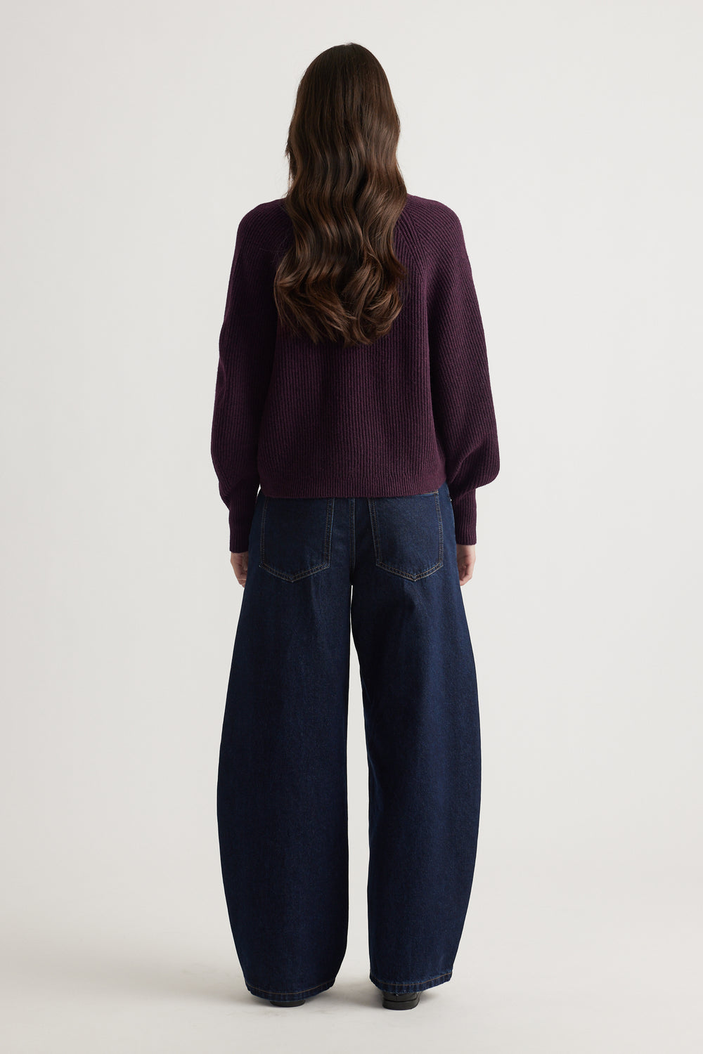 Woman wearing a deep plum knit cardigan with balloon sleeves paired with wide-leg dark blue denim jeans