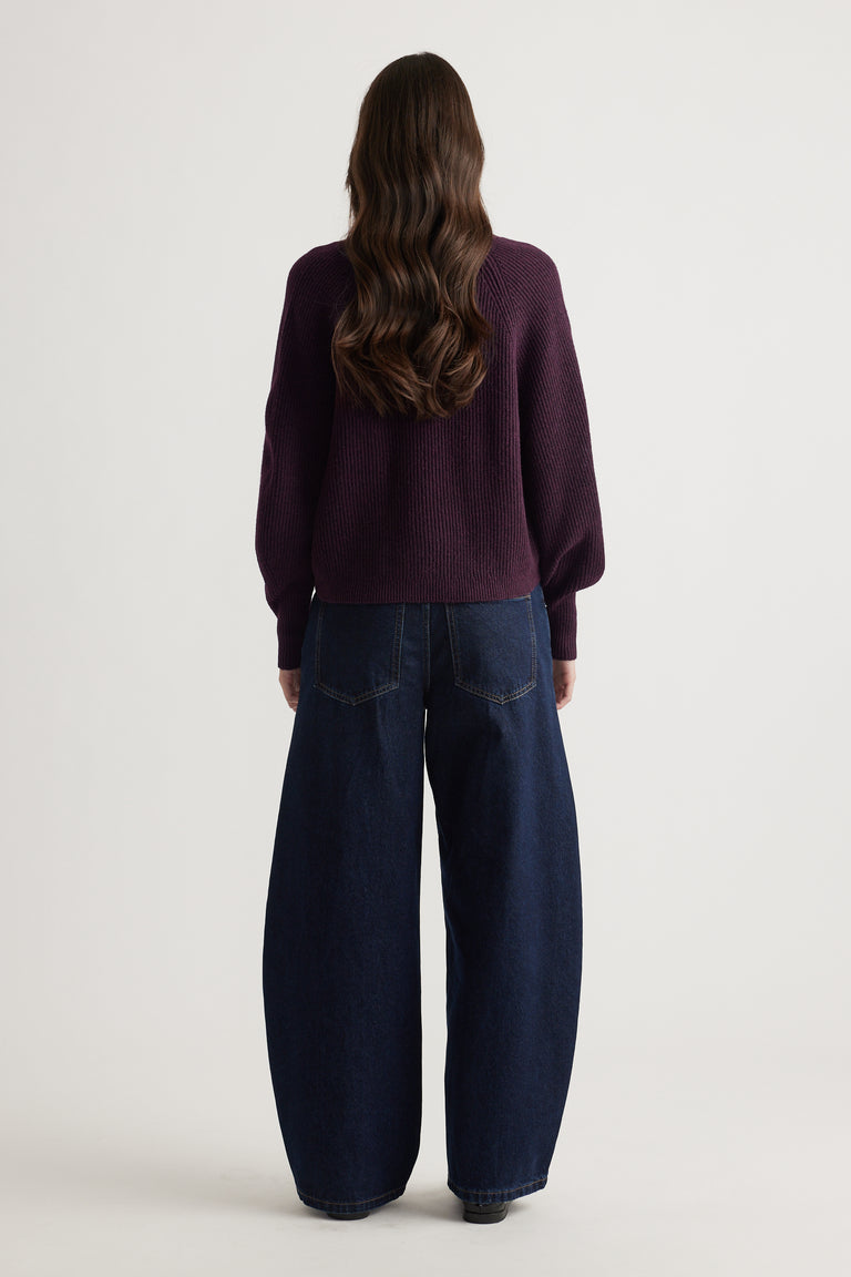Woman wearing a deep plum knit cardigan with balloon sleeves paired with wide-leg dark blue denim jeans