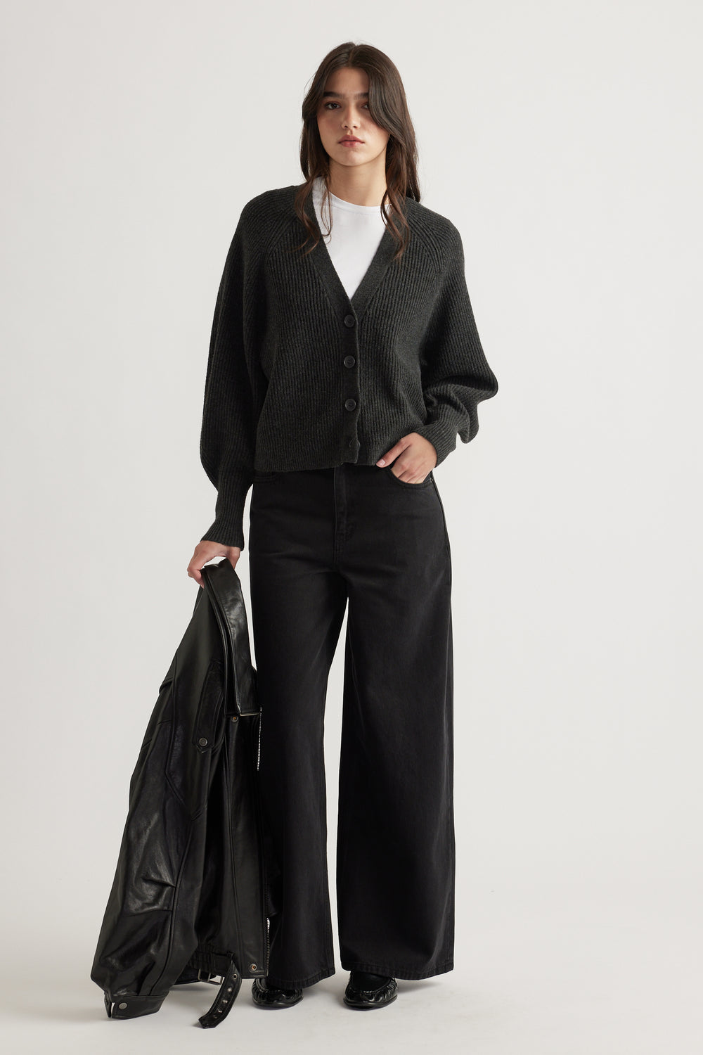Woman wearing a charcoal knit cardigan with balloon sleeves, paired with wide-leg black pants and holding a leather jacket.