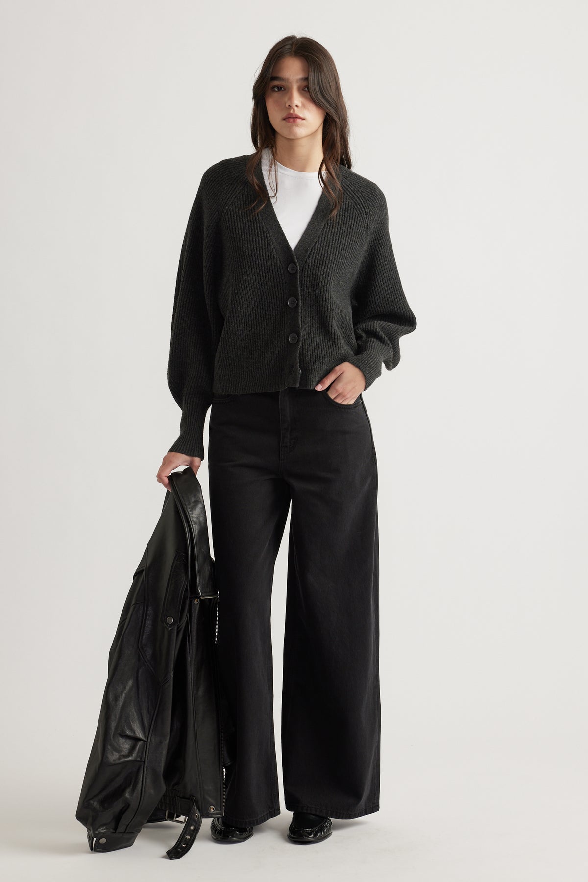 Woman wearing a charcoal knit cardigan with balloon sleeves, paired with wide-leg black pants and holding a leather jacket.