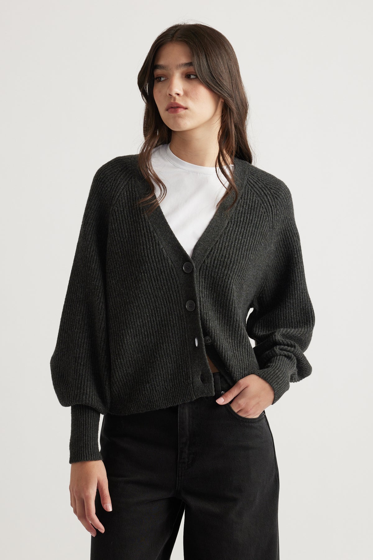 Woman wearing a charcoal knit cardigan with balloon sleeves over a white tee paired with black high-waisted pants