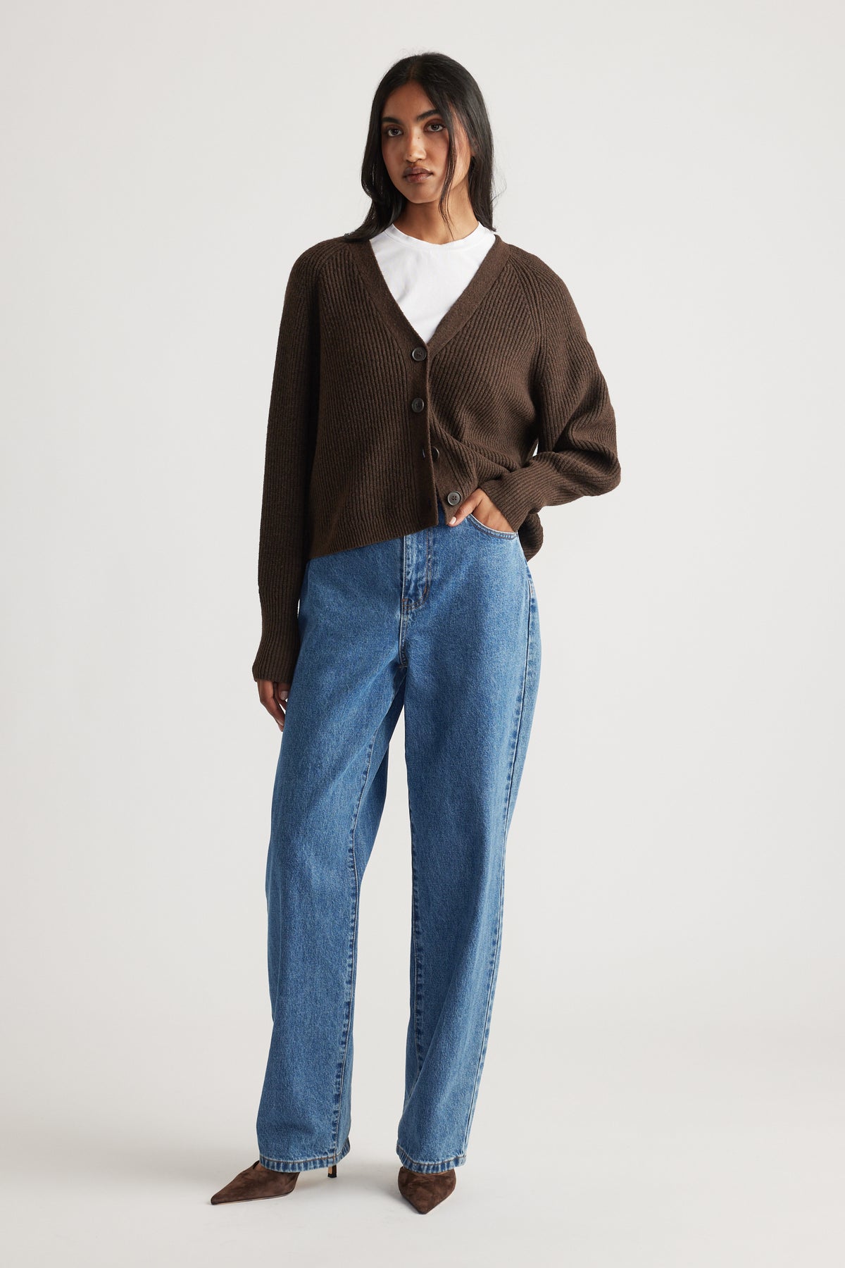 Woman wearing a relaxed dark brown knit cardigan with buttons, styled with a white tee, straight-leg blue jeans, and brown shoes