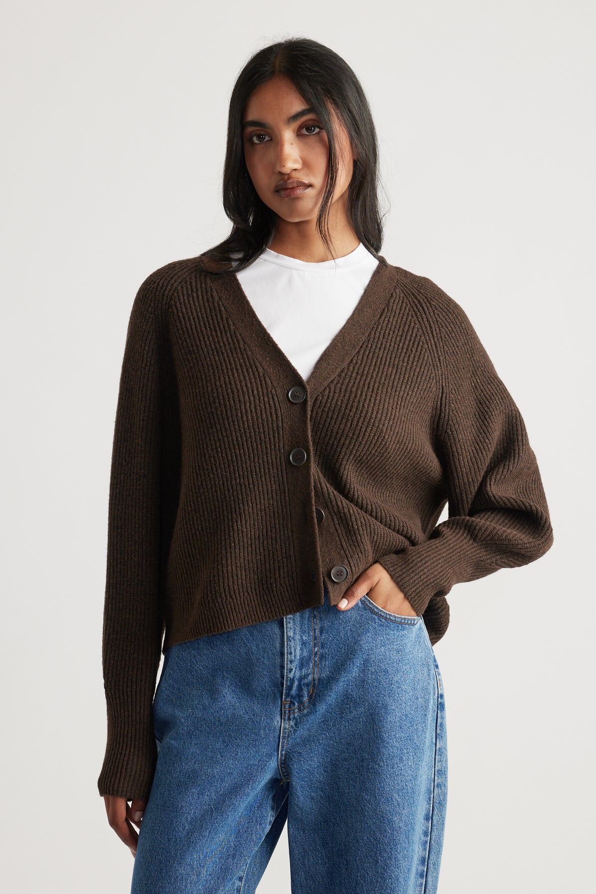 Model wearing a cozy dark brown button-up knit cardigan layered over a white top paired with mid-blue casual jeans