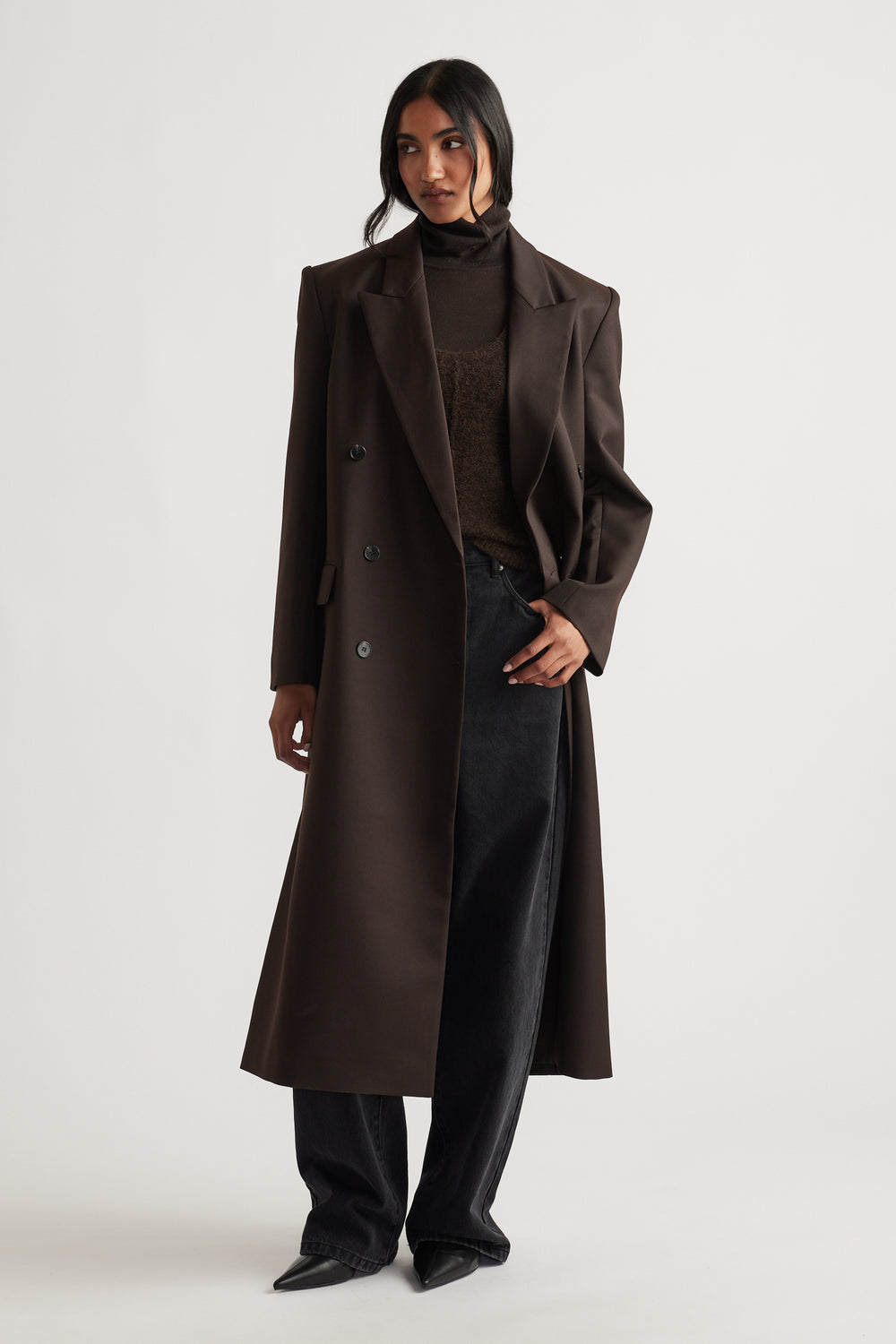 Woman wearing Ella Blazer Coat in rich brown with structured shoulders and longline fit paired with black wide-leg jeans and pointed boots