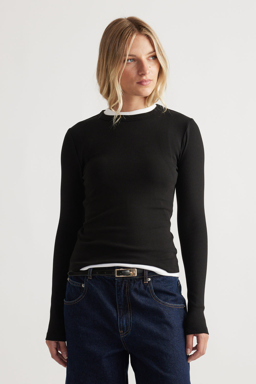 Blonde woman wearing a fitted black long-sleeve top layered over a white shirt paired with dark blue denim jeans