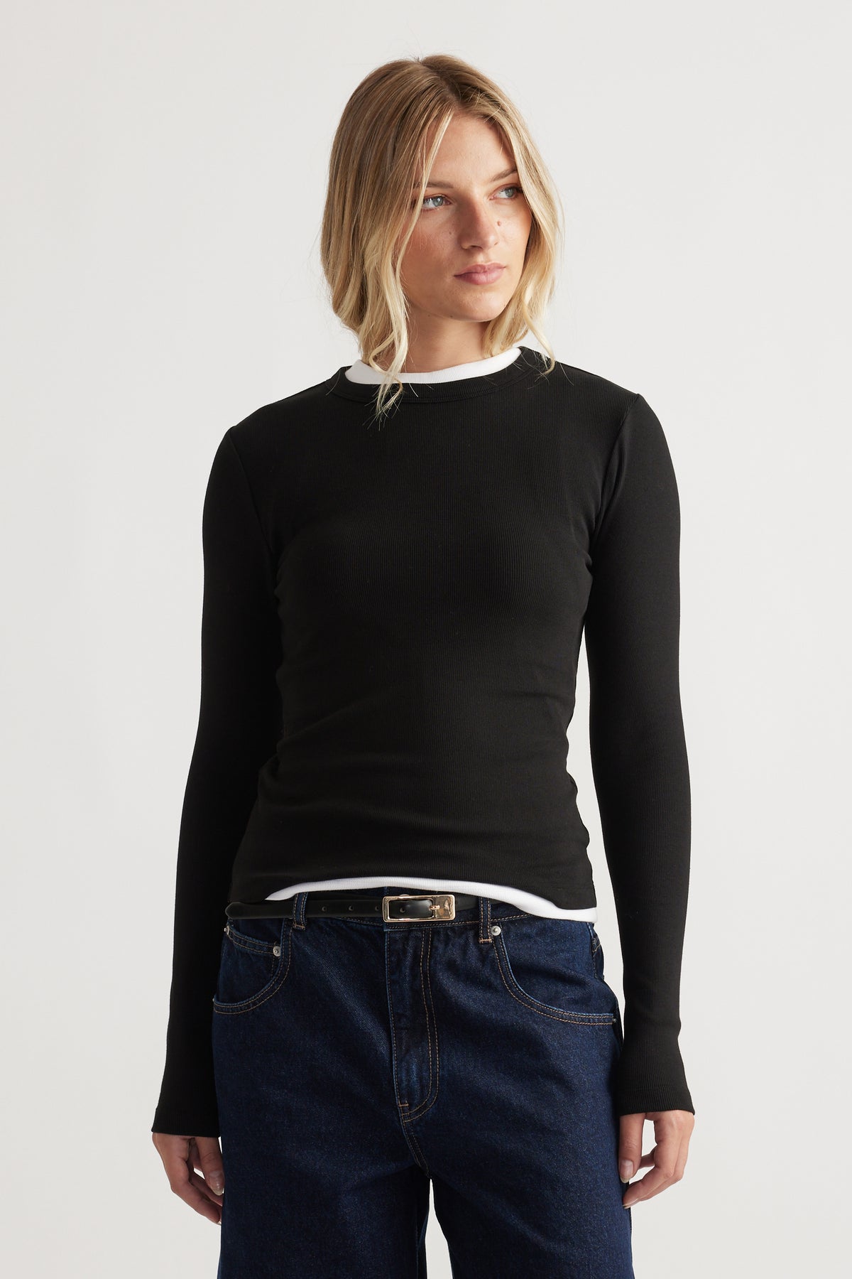 Blonde woman wearing a fitted black long-sleeve top layered over a white shirt paired with dark blue denim jeans
