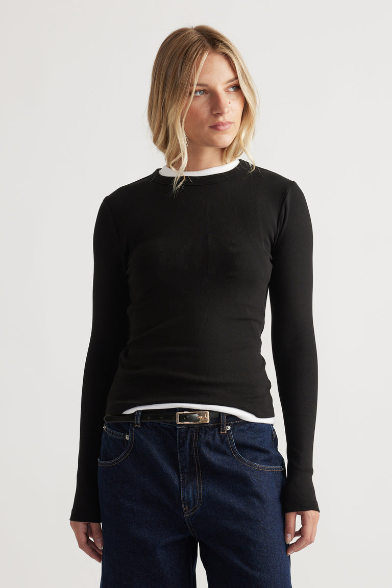 Blonde woman wearing a fitted black long-sleeve top layered over a white shirt paired with dark blue denim jeans