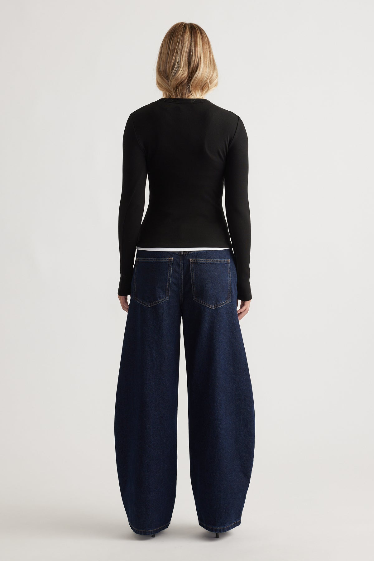 Woman wearing a fitted black long-sleeve top paired with wide-leg dark indigo denim jeans seen from the back