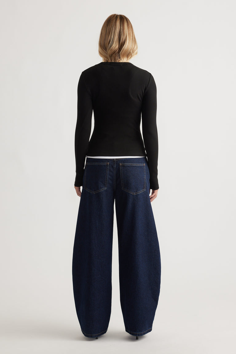 Woman wearing a fitted black long-sleeve top paired with wide-leg dark indigo denim jeans seen from the back