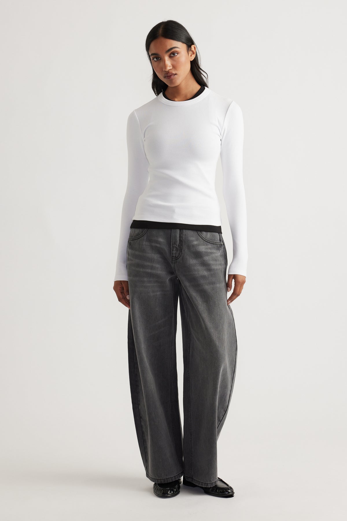 Woman wearing a fitted white long sleeve top layered over a black tee paired with loose-fitting faded black denim pants