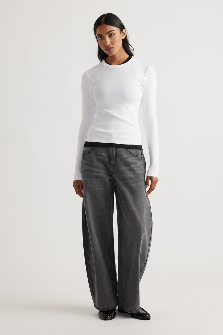 Woman wearing a fitted white long sleeve top layered over a black tee paired with loose-fitting faded black denim pants