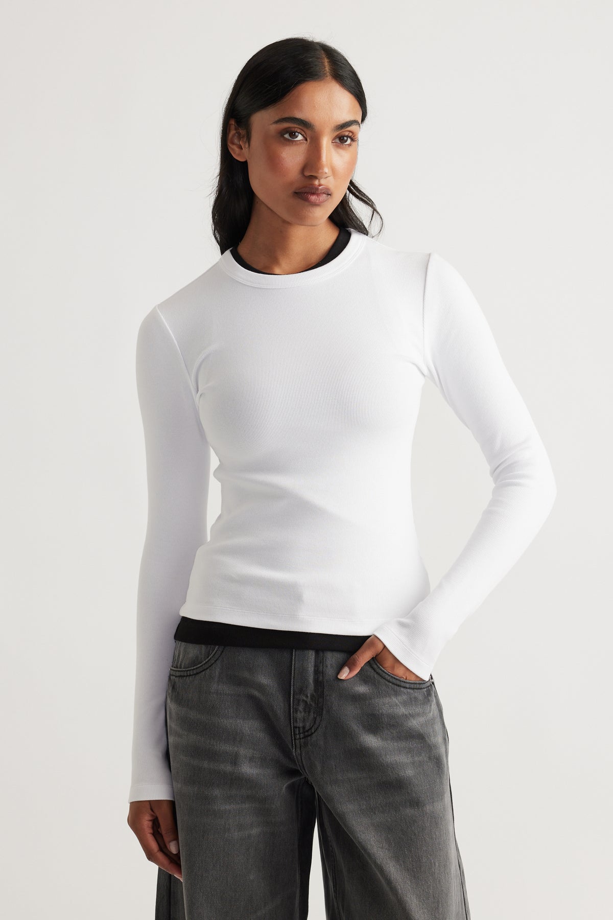 Woman wearing a fitted white long sleeve top layered over a black tee paired with loose faded black jeans