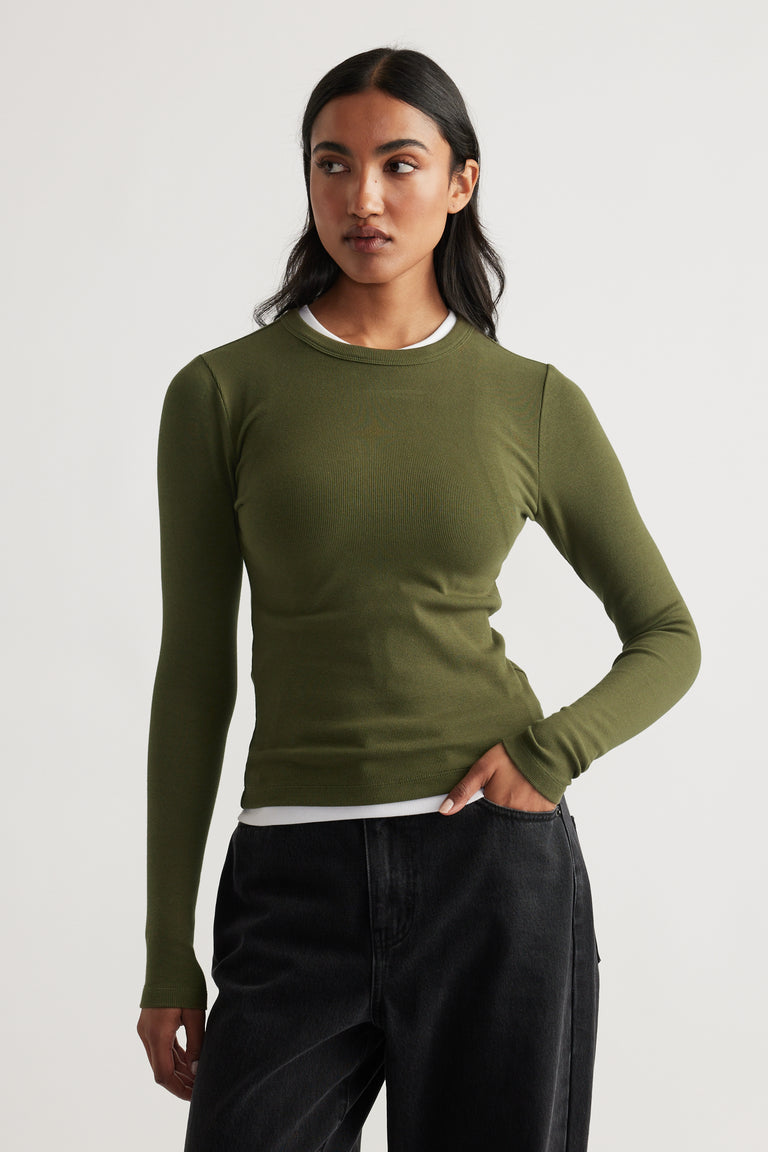 Slim fit olive long sleeve top layered over white tee, styled with relaxed black denim jeans for a casual look