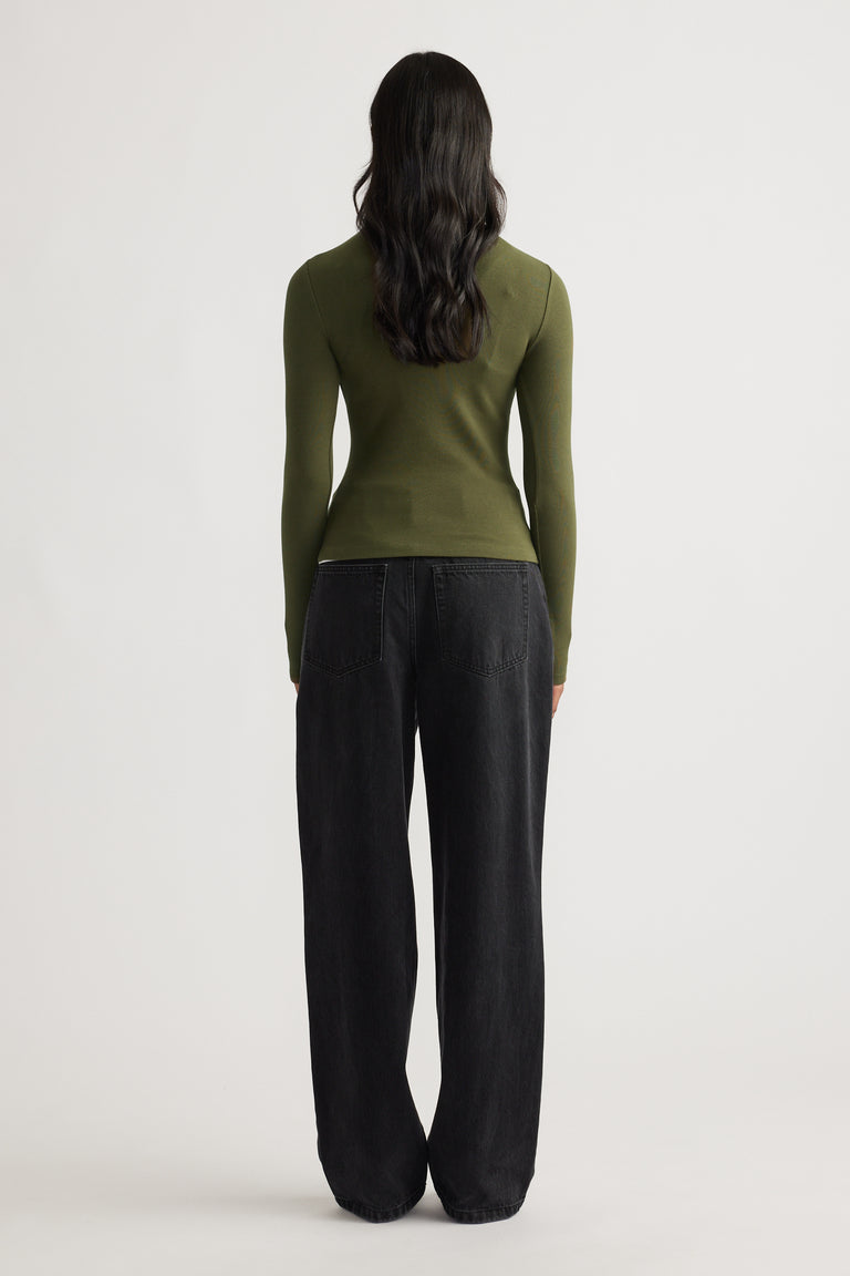 Woman wearing a fitted olive green long sleeve top paired with loose black wide-leg denim jeans against a plain background.