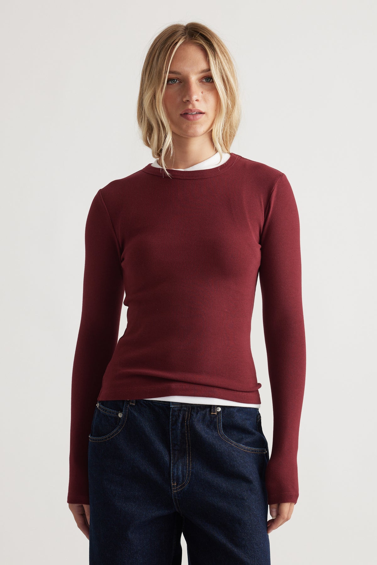 Slim-fit long sleeve top in deep red layered over a white crew neck, paired with classic dark blue denim jeans
