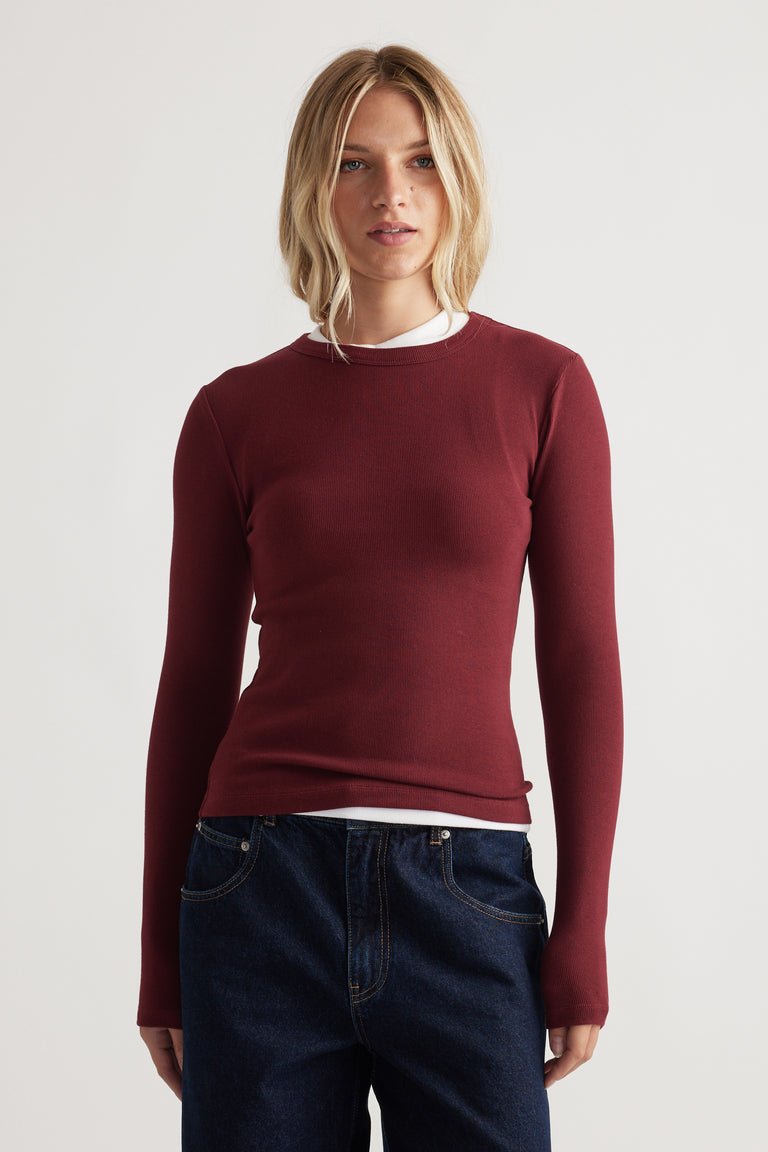 Slim-fit long sleeve top in deep red layered over a white crew neck, paired with classic dark blue denim jeans