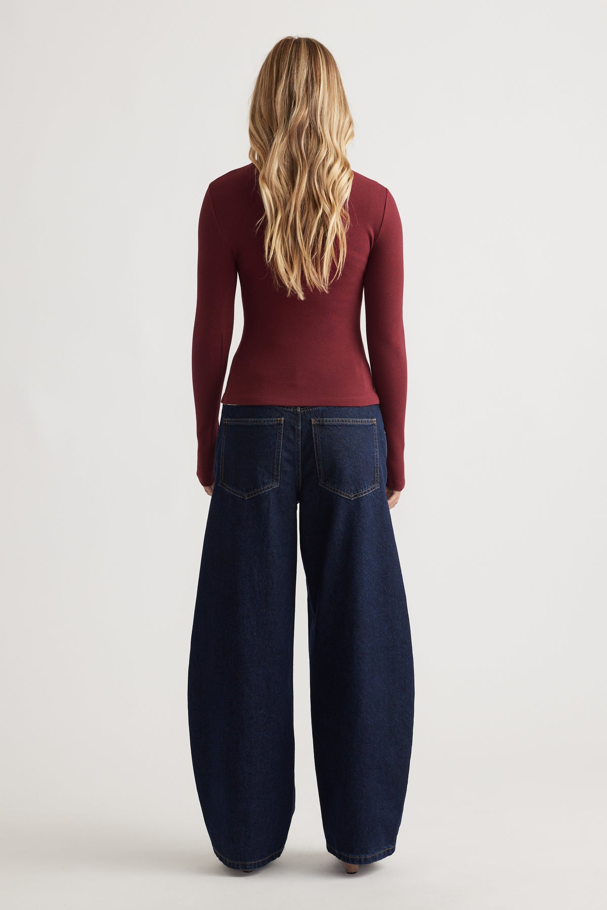 Back view of a fitted deep red long sleeve top paired with wide-leg dark indigo denim jeans for a sleek look