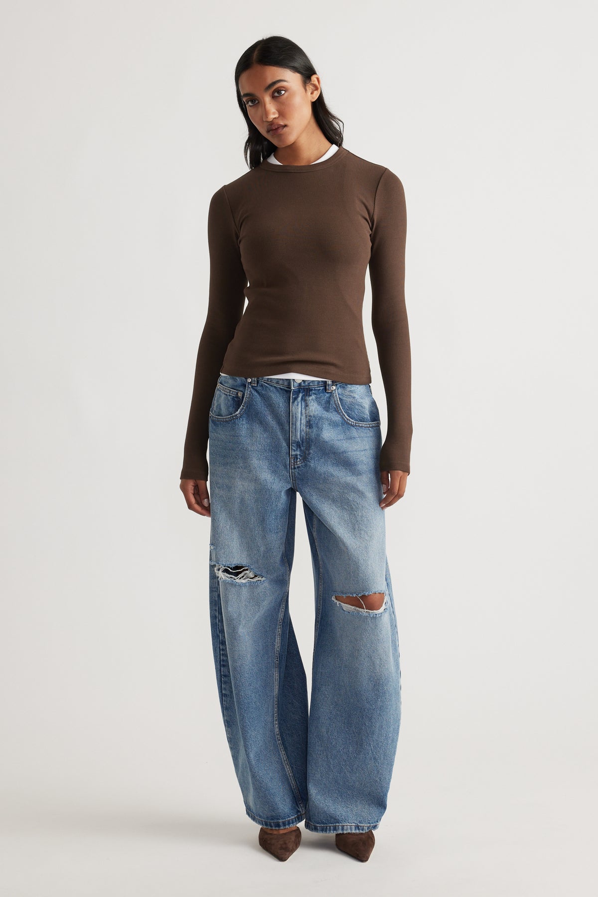 Front view of a fitted brown long sleeve top layered over a white tee, paired with relaxed ripped wide-leg denim jeans and brown shoes