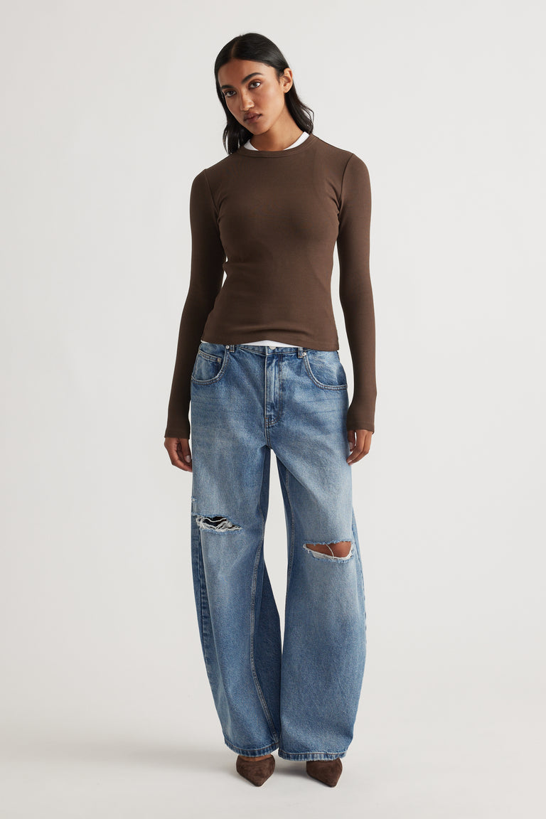 Front view of a fitted brown long sleeve top layered over a white tee, paired with relaxed ripped wide-leg denim jeans and brown shoes