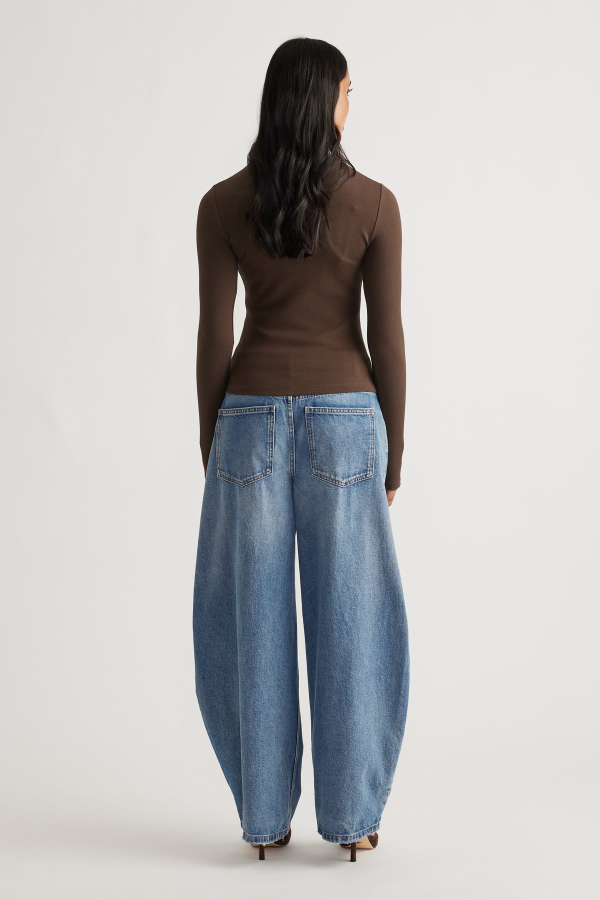 Back view of a slim-fit brown long sleeve top paired with relaxed wide-leg blue denim jeans and heels.