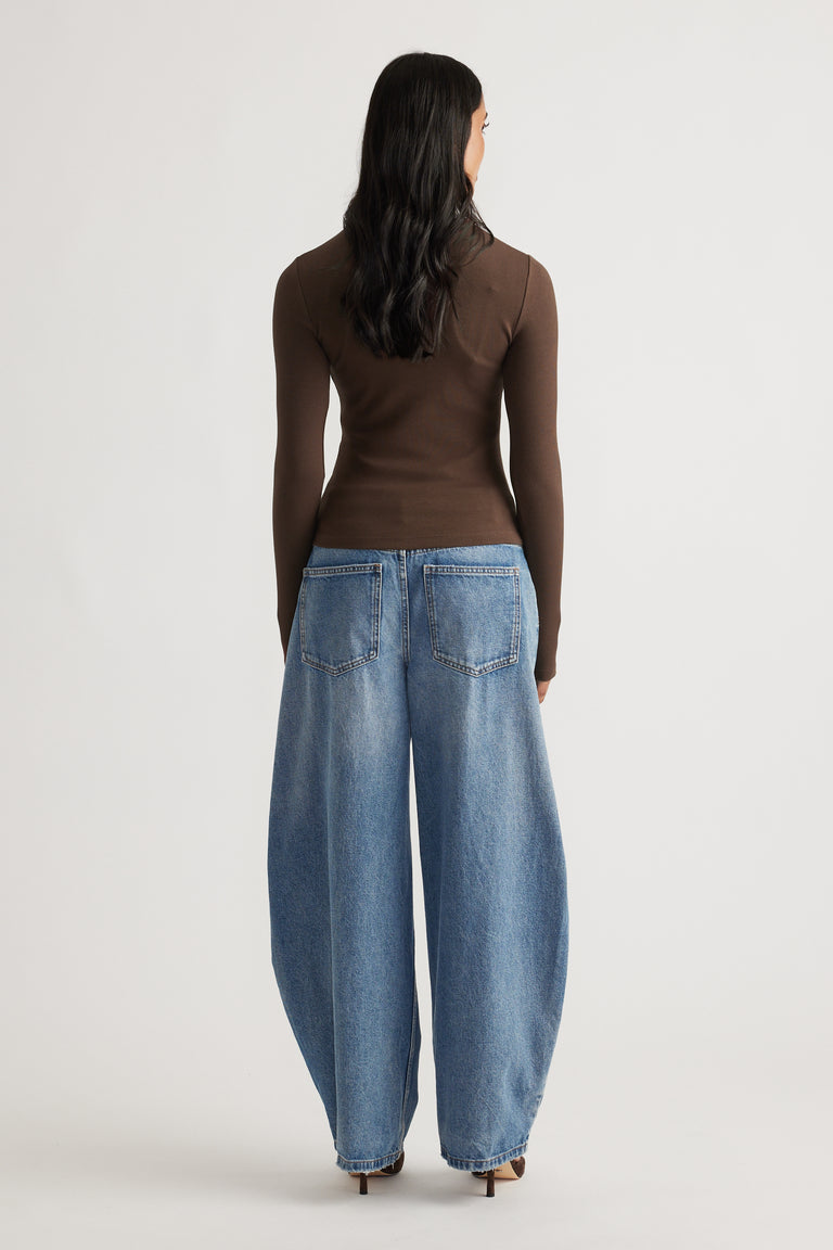 Back view of a slim-fit brown long sleeve top paired with relaxed wide-leg blue denim jeans and heels.