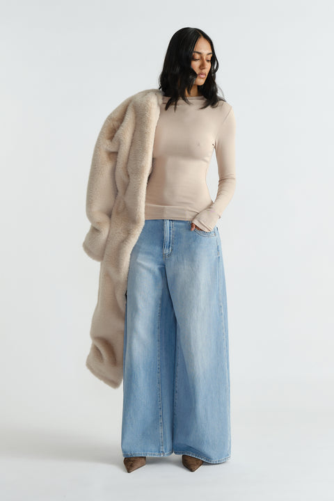 Woman wearing a fitted beige long sleeve top paired with wide-leg light wash denim jeans and holding a plush coat.