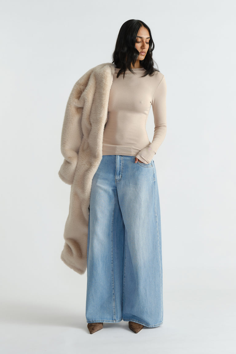 Woman wearing a fitted beige long sleeve top paired with wide-leg light wash denim jeans and holding a plush coat.